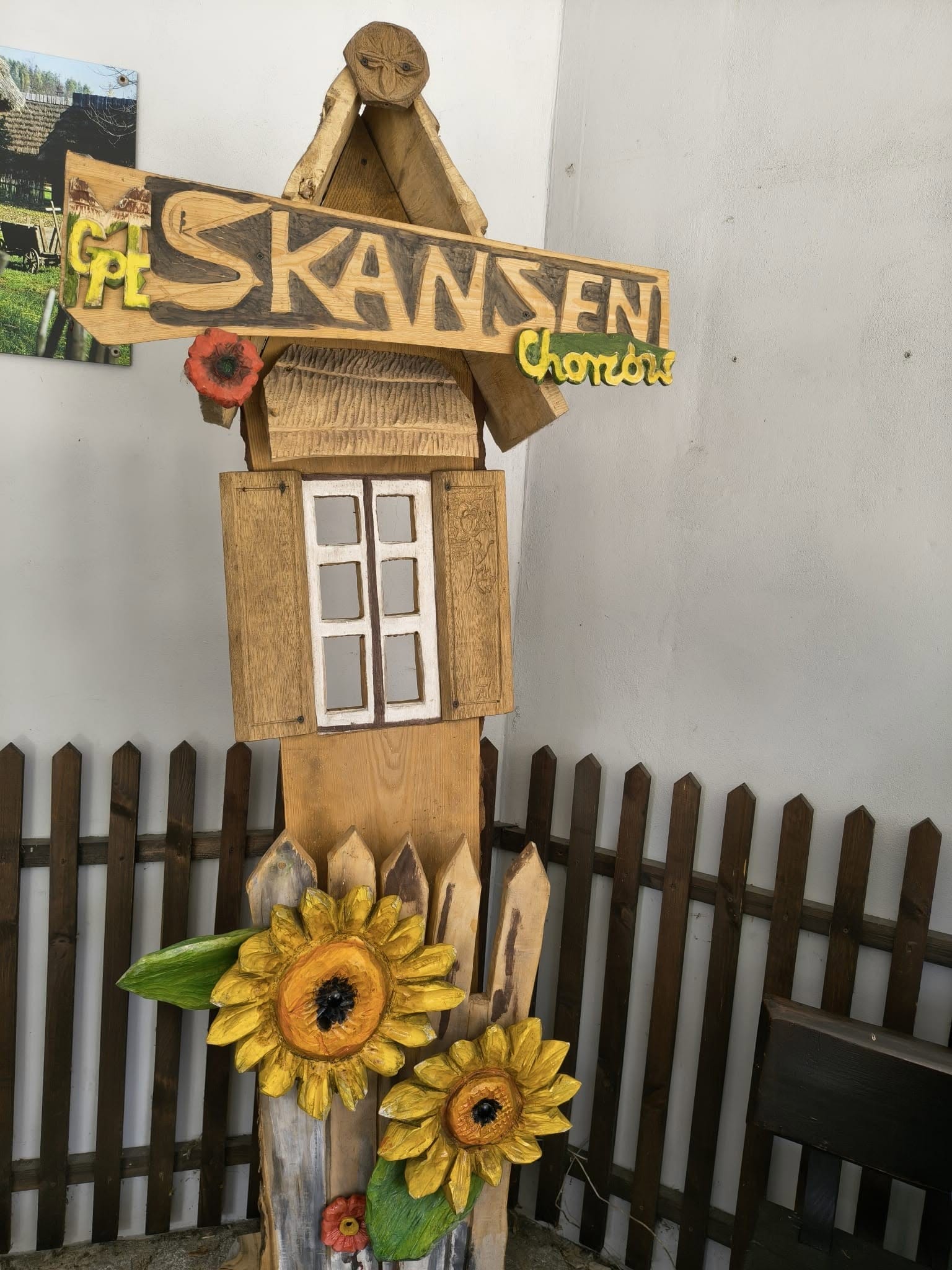 Rzeźbiona drewniana tablica z napisem SKANSEN, ozdobiona motywem słoneczników.
