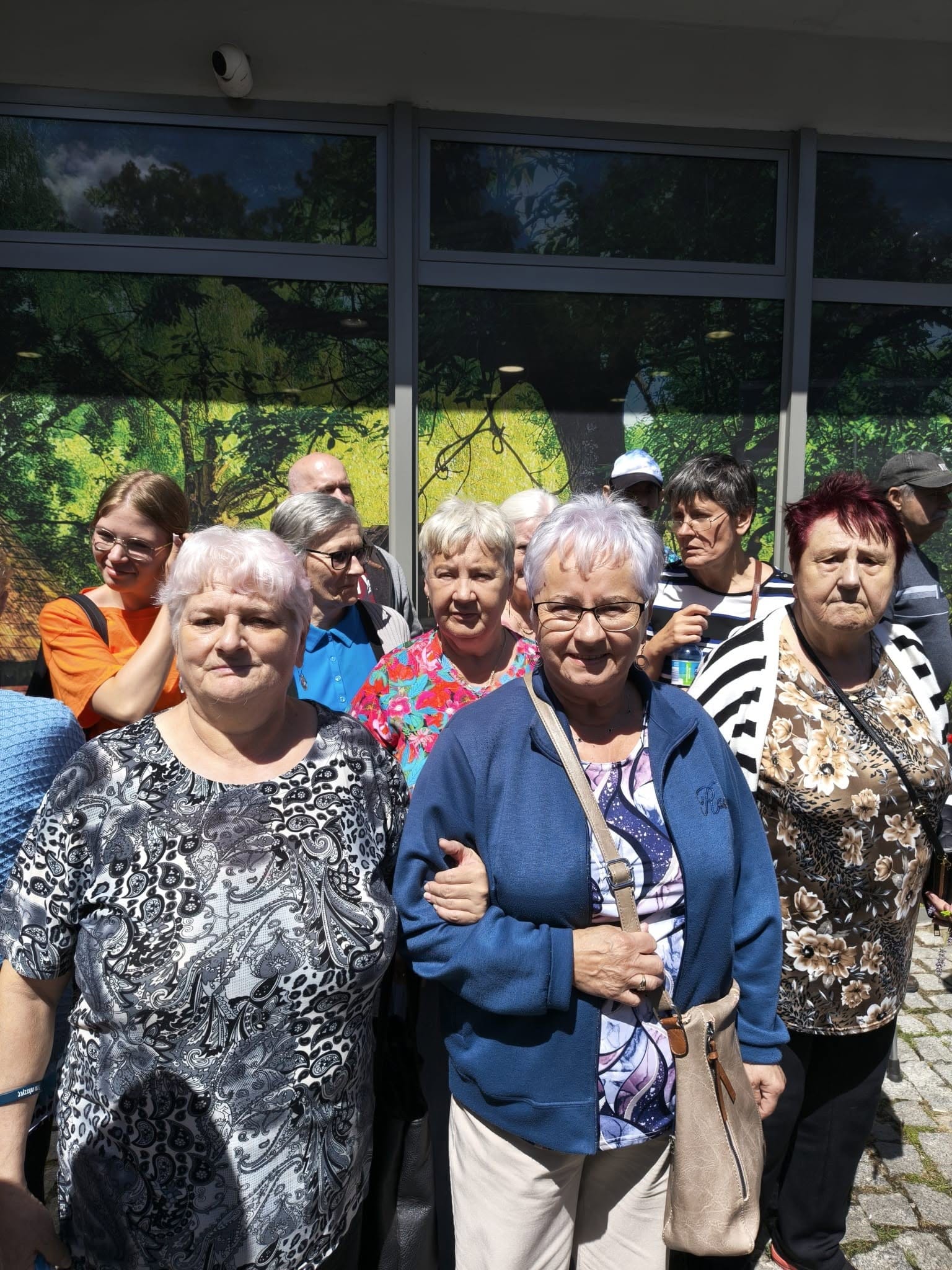 Uczestniczki wycieczki pozujące razem przed przeszklonym budynkiem.