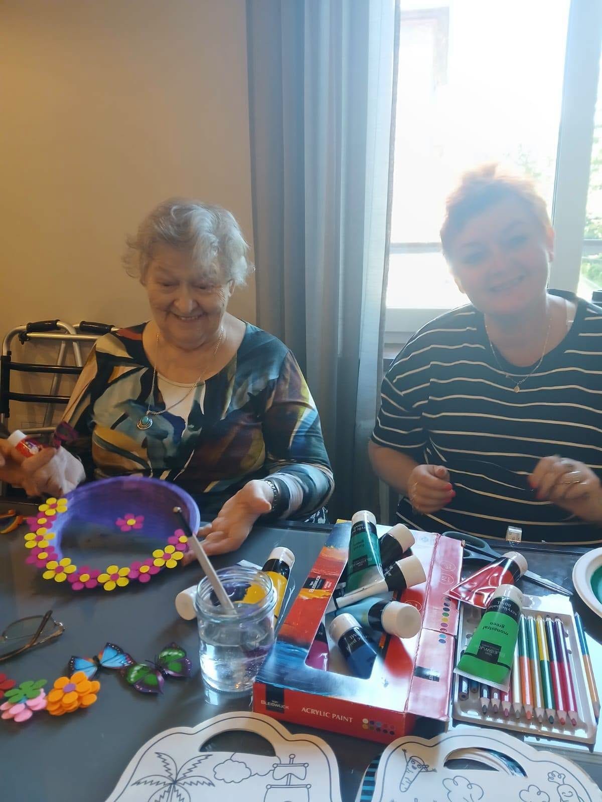 Uśmiechnięta seniorka i wolontariuszka podczas tworzenia prac plastycznych.