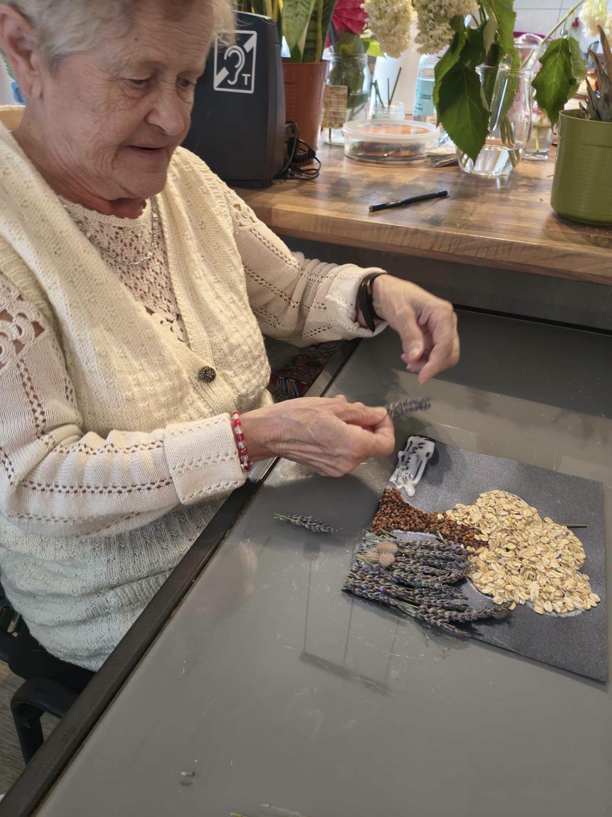 Seniorka układająca suszoną lawendę na pracy plastycznej z ziaren.