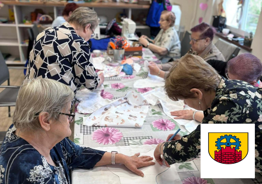 Seniorki pracują przy długim stole nad materiałami do szycia.