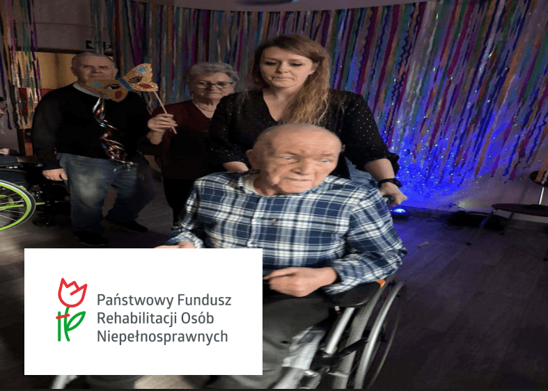 Senior na wózku i opiekunowie podczas imprezy karnawałowej oraz logo PFRON w rogu.