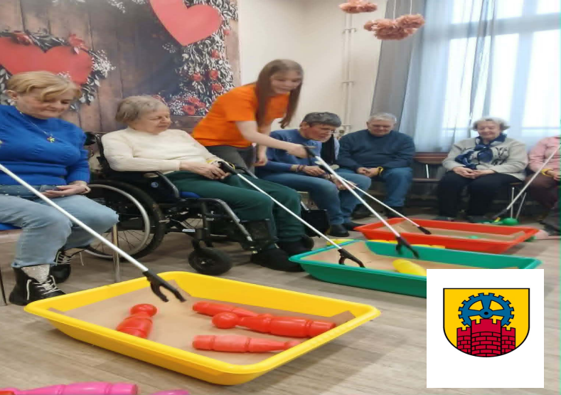 Seniorzy i osoba na wózku grają w kręgle za pomocą chwytaków. W rogu herb Zabrza.